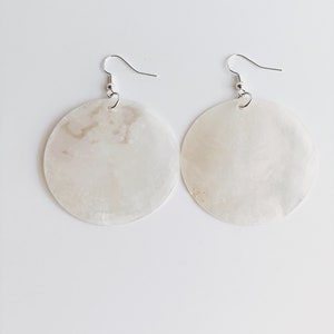 May include: A pair of white shell earrings with silver hooks. The earrings are round and have a natural, organic look.