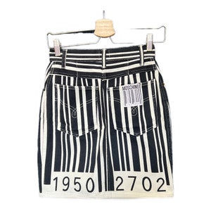 Könnte beinhalten: Schwarzer und weißer gestreifter Jeans-Minirock mit einem Moschino-Etikett und einem Barcode auf der Gesäßtasche. Der Rock hat eine hohe Taille und eine gerade Passform. Am Saum des Rocks sind die Zahlen 1950 2702 aufgedruckt.