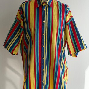 May include: A short-sleeved button-down shirt with vertical stripes in red, yellow, blue, and green. The shirt has a classic collar and gold-colored buttons. The fabric appears to be cotton or a similar material.