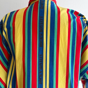 May include: A colorful striped shirt with vertical stripes in red, yellow, blue, and green. The text "ROCK'N ROYALTY" is printed vertically on the back. The shirt has a button-down collar and short sleeves.