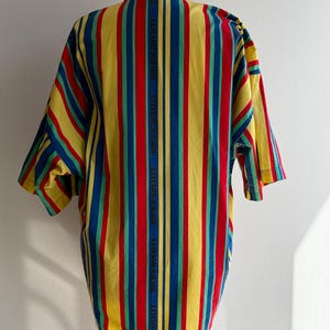 May include: A short-sleeved shirt with vertical stripes in yellow, red, blue, and green. The shirt has a button-down collar and the text "ROCK'S ROYALTY" printed vertically on the back.