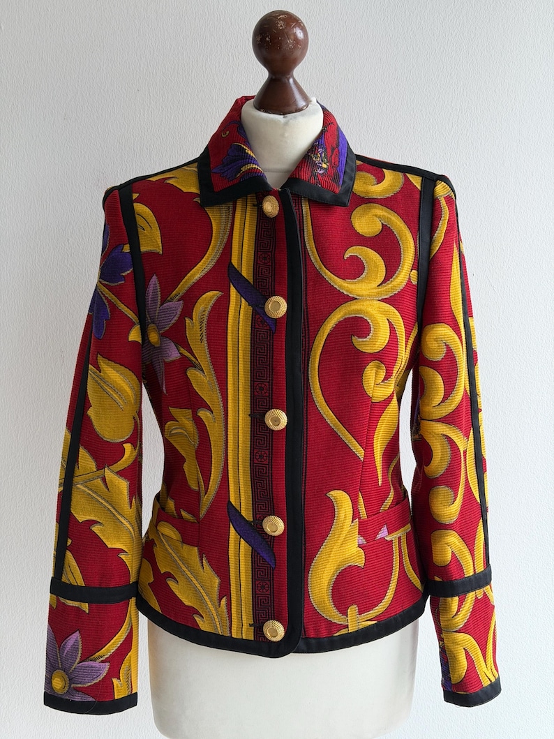 May include: A red jacket with a vibrant yellow and purple floral pattern. The jacket features black trim, gold buttons, and a classic collar. The design includes a vertical stripe with a geometric pattern.