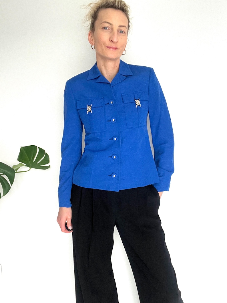 May include: A royal blue blazer with long sleeves, a button-up front, and two flap pockets with decorative gold buttons.