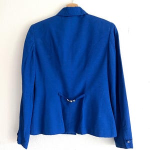 May include: A royal blue blazer with a single button closure and a small metal buckle detail on the back.