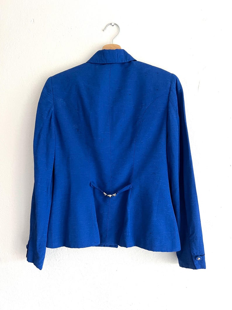 May include: A royal blue blazer with a single button closure and a small metal buckle detail on the back.