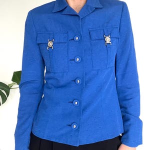 May include: A royal blue blazer with a button-up front and two flap pockets with silver accents. The blazer has a slim fit and is made of a textured fabric.