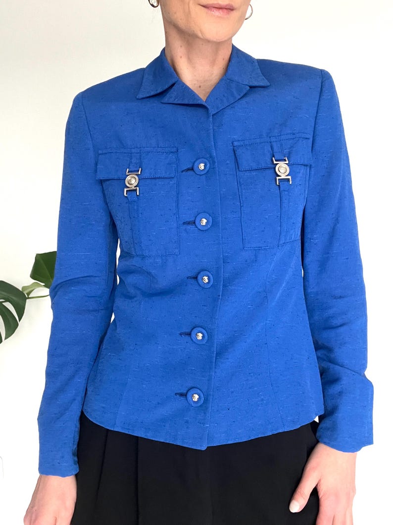 May include: A royal blue blazer with a button-up front and two flap pockets with silver accents. The blazer has a slim fit and is made of a textured fabric.