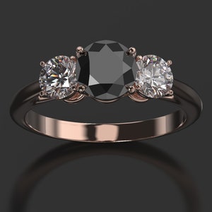Pode incluir: Um anel de tr&ecirc;s pedras com um grande diamante preto oval no centro e dois diamantes redondos menores de cada lado. O anel &eacute; de ouro rosa.