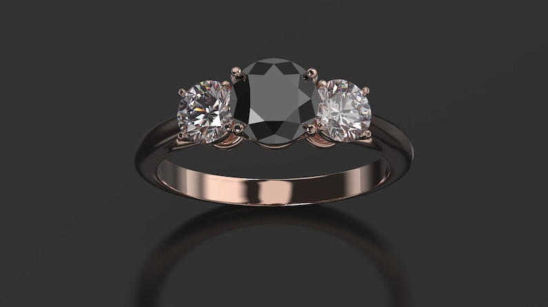 Pode incluir: Um anel de tr&ecirc;s pedras com um grande diamante preto oval no centro e dois diamantes redondos menores de cada lado. O anel &eacute; de ouro rosa.