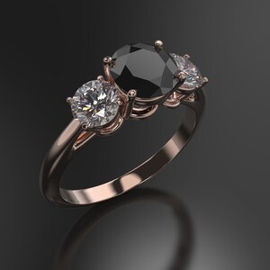 Pode incluir: Um anel de noivado de tr&ecirc;s pedras com um grande diamante preto no centro e dois diamantes brancos menores de cada lado. O anel &eacute; engastado em ouro rosa.