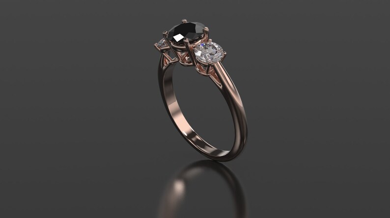 Pode incluir: Um anel de noivado de ouro rosa com uma pedra central de diamante preto e dois diamantes brancos menores de cada lado.