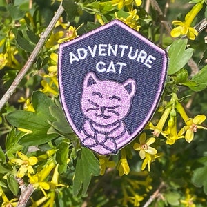 May include: A black and white iron-on patch with a pink cartoon cat and the text "Adventure Cat".