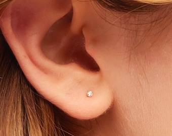 May include: A close-up of a person's ear with a small diamond stud earring. The earring is set in a gold setting.
