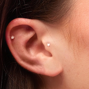 May include: Close-up of a person's ear with two small silver star stud earrings.