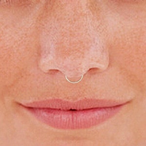 May include: A close-up of a person's face with a small, silver hoop nose ring.