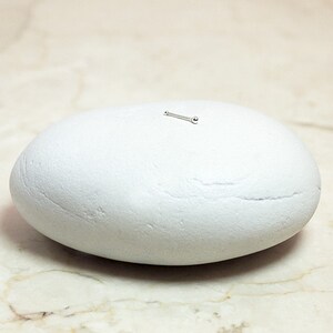 May include: A small silver nose stud with a round ball on the end. The stud is sitting on a white rock.