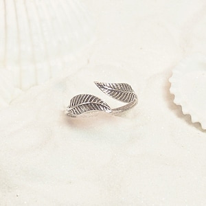 May include: A silver ring with two leaf designs. The ring is open and adjustable.