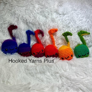 May include: Six crocheted musical note plushies in a rainbow of colors. The plushies are arranged in a row from left to right, starting with blue, purple, red, orange, yellow, and green.