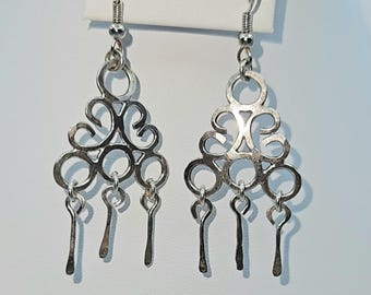 Peut inclure: Une paire de boucles d'oreilles pendantes argentées. Chaque boucle d'oreille présente un motif ajouré avec des formes tourbillonnantes et des breloques en forme de goutte d'eau. Les boucles d'oreilles sont suspendues à un simple crochet.