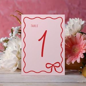 Chiffres de table roses et rouges, marque-places de mariage de forme ondulée, noeud fantaisiste tout en courbes rétro des années 70