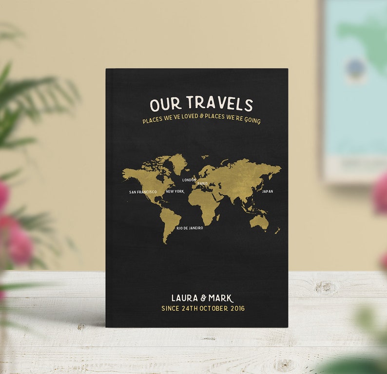 May include: A black world map print with gold-colored continents and the text "OUR TRAVELS". The map highlights cities like London, Paris, and New York. Below the map is the text "LAURA & MARK SINCE 24TH OCTOBER 2016".