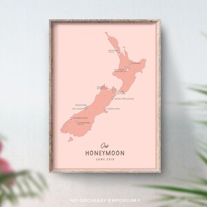May include: A framed print showing a coral-coloured map of New Zealand, with location markers. The text "Our Honeymoon June 2018" is below the map. The frame is light wood. The print is a decorative item.