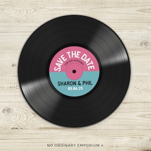 May include: A black vinyl record with a pink and blue circle in the centre. The circle says "Save the Date for our Wedding!" with the names "Sharon & Phil" and the date "05.06.25".