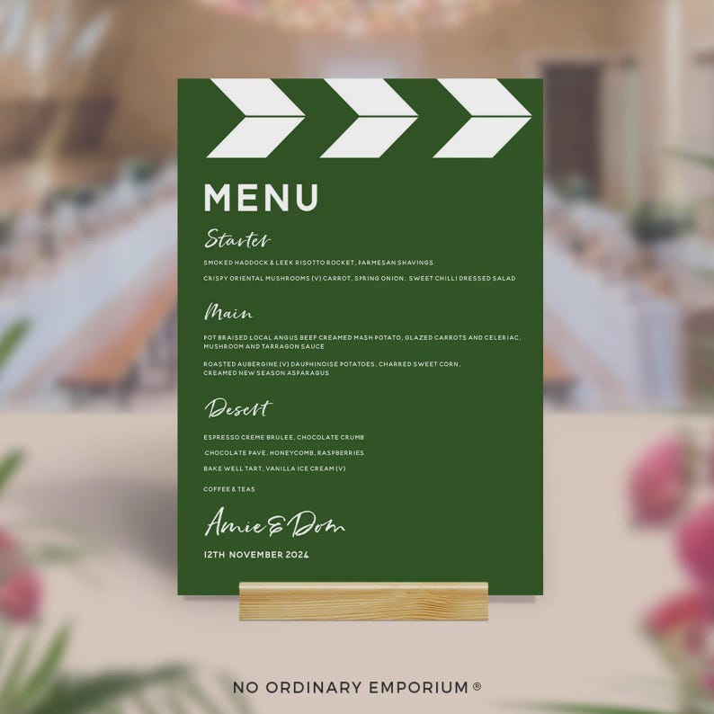 May include: A green menu card with white text, held by a wooden stand. The menu lists starters, main courses, and desserts. The menu is for Amie & Dom, dated 12th November 2024. The top of the card features a white arrow design.
