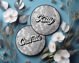 Puede incluir: Dos tarjetas de lugar de estilo bola de discoteca plateadas con los nombres "Kitty" y "Charlie" escritos en letra cursiva negra.