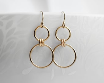 May include: Gold double circle earrings with a knotted detail. The earrings are made of a thin, delicate wire.