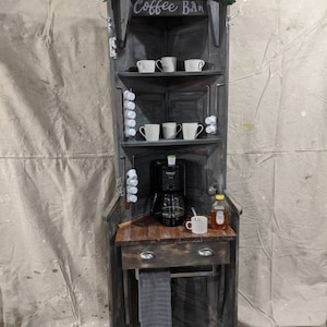 May include: A coffee bar made from a repurposed door with a wooden countertop, a coffee maker, a drawer, a towel rack, and a sign that reads 