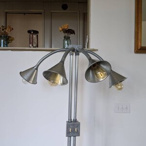 以下が含まれることがあります： 5つの調節可能な照明器具が付いたシルバーのフロアランプ。各器具は、漏斗型のシェードと電球が付いています。ランプは、シルバーの金属製のベースとシルバーの金属製のポールが付いています。