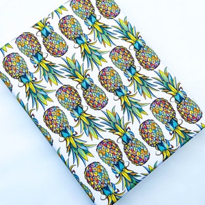 May include: White wrapping paper with a repeating pattern of colorful pineapples. The pineapples are drawn in a stylized manner with yellow, orange, red, blue, and green colors.