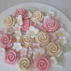 Könnte beinhalten: Eine Sammlung von rosa und cremefarbenen Fondantrosen und kleinen Blüten, perfekt zum Dekorieren von Kuchen oder Cupcakes.