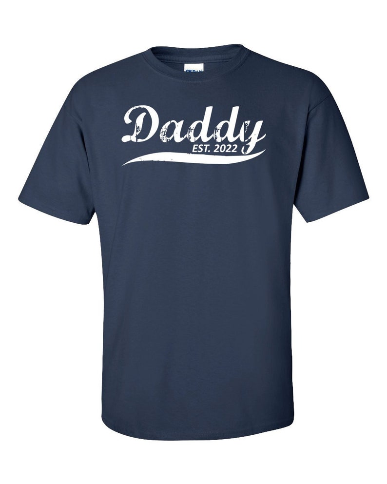 May include: Navy blue t-shirt with white text that reads "Daddy Est. 2022" in a vintage style font.