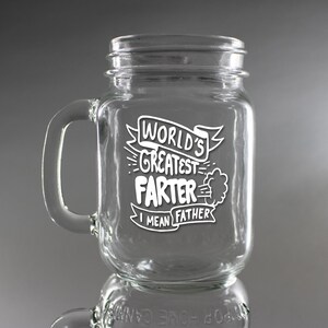 Peut inclure: Une tasse en verre transparent de type bocal à confiture avec une anse blanche. La tasse est gravée avec le texte "World's Greatest Farter I mean Father" avec un nuage de dessin animé et une ligne représentant un pet.