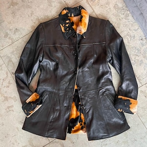 May include: A black leather jacket with a brown and black fur collar and cuffs. The jacket has a button closure and two pockets.