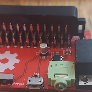 May include: A red circuit board with the text "open hardware" and a black connector with a row of pins. The board also has a green connector, a black connector with a silver connector, and a small black switch labeled "bypass".