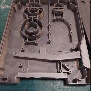 May include: A gray 3D printed plastic model with intricate details and a textured surface. The model features a series of circular and rectangular shapes, creating a complex design.