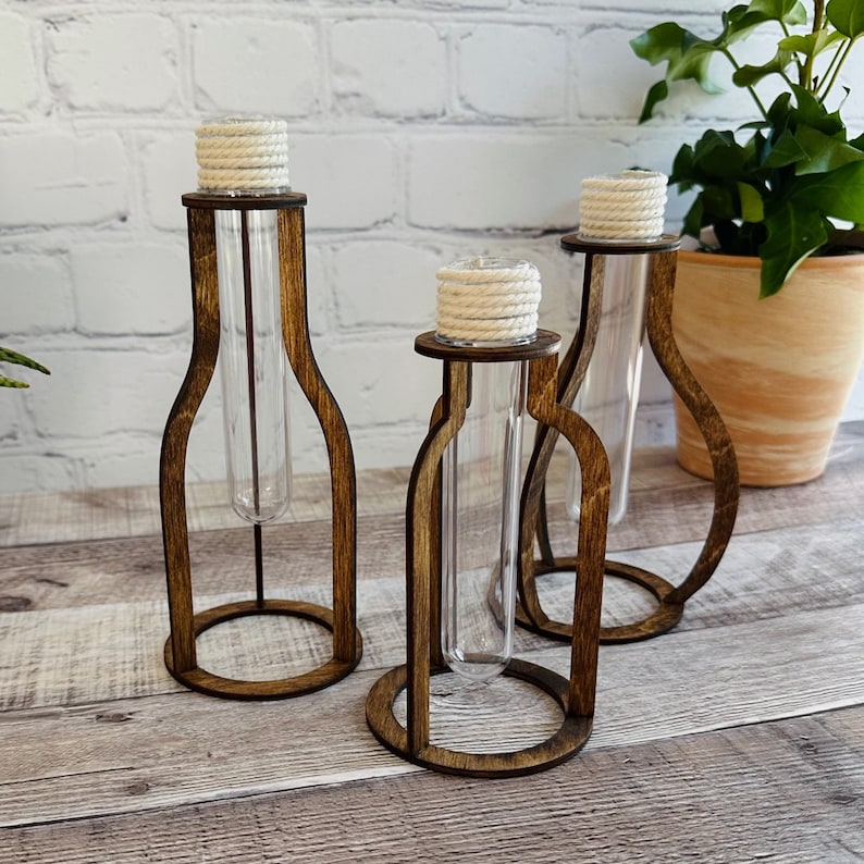 May include: Three wooden test tube holders with rope accents. The holders are in the shape of a bottle and are made of dark brown wood. The test tubes are clear glass.