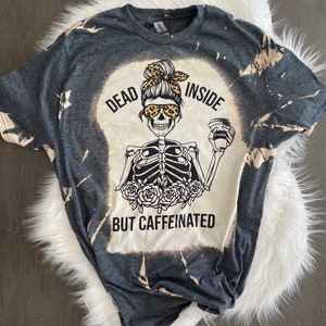 May include: A dark gray t-shirt with a bleached design featuring a skeleton holding a coffee cup. The text on the shirt reads "Dead Inside But Caffeinated".