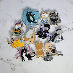May include: A set of 12 enamel pins featuring cats in various poses and designs. The pins are colorful and feature a variety of styles, including a cat with a lute, a cat with a unicorn horn, and a cat with a crown.