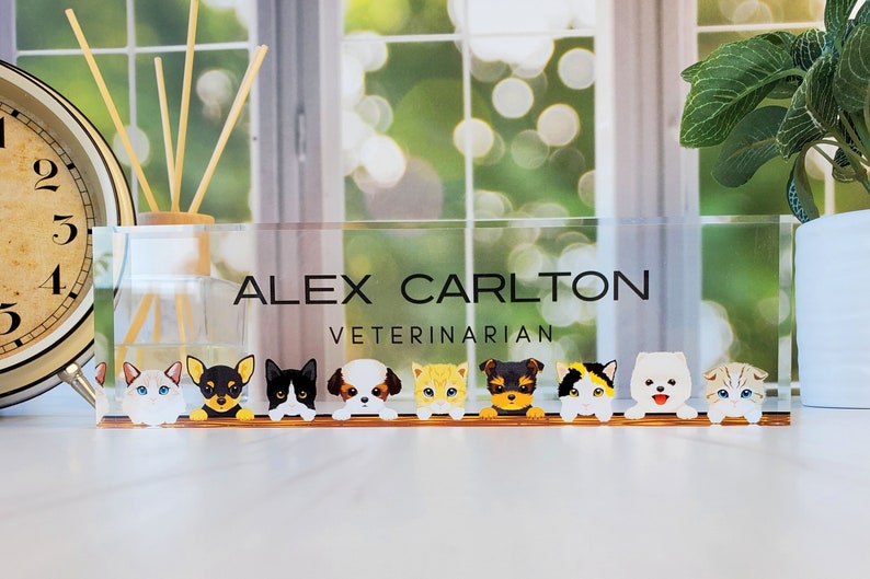 Peut inclure: Une plaque de nom de bureau en acrylique transparente avec le texte "ALEX CARLTON VETERINARIAN" et une rang&eacute;e d'animaux de dessin anim&eacute;, y compris des chats et des chiens, qui regardent par-dessus le haut.