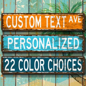May include: Three rectangular wooden signs with white text against a distressed background. The top sign is orange and reads "CUSTOM TEXT AVE". The middle sign is blue and says "PERSONALIZED". The bottom sign is dark blue and says "22 COLOUR CHOICES".