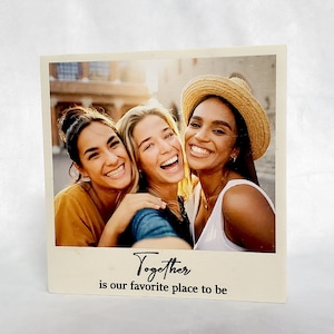 May include: Three friends smiling and taking a selfie together. The photo is printed on a white background with a beige border and the text "Together is our favorite place to be".