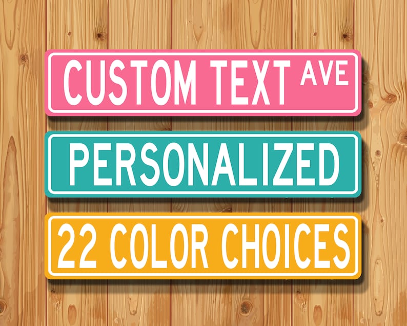 May include: Three colourful street signs with white text against a wooden background. The top sign is pink and reads "CUSTOM TEXT AVE". The middle sign is teal and says "PERSONALIZED". The bottom sign is yellow and states "22 COLOUR CHOICES".