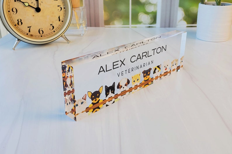 Peut inclure: Une plaque de nom de bureau en acrylique transparente avec un fond blanc et du texte noir. Le texte indique "Alex Carlton, V&eacute;t&eacute;rinaire". La plaque est d&eacute;cor&eacute;e d'une bordure de chiens et de chats de dessin anim&eacute;.