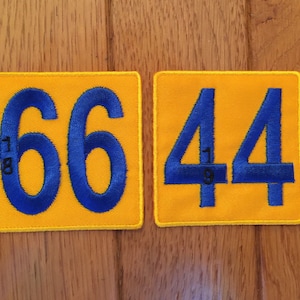 May include: Two yellow fabric patches with blue numbers. The left patch has the number 66 and the right patch has the number 44.