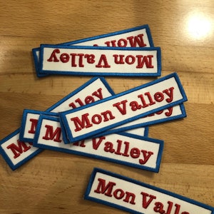 May include: A stack of white fabric patches with blue and red embroidery. The patches read "Mon Valley" in red lettering.