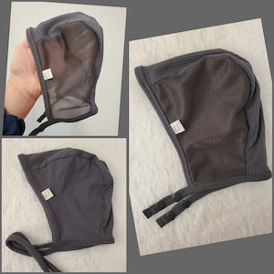 May include: Gray hooded baby hat with a mesh panel and ties. The hat has a label that says "Made with Love".